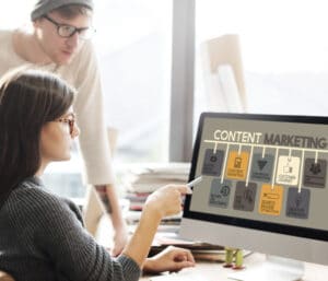 Two people look at computer screen with the words "content marketing" on it. 