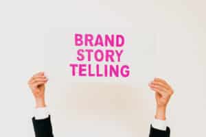 This image shows two hands holding up a sign with “brand storytelling” written on it. Storytelling is one of our social media marketing tips for businesses.