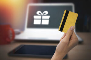 A hand in front of a computer about to make a purchase holding a gift card